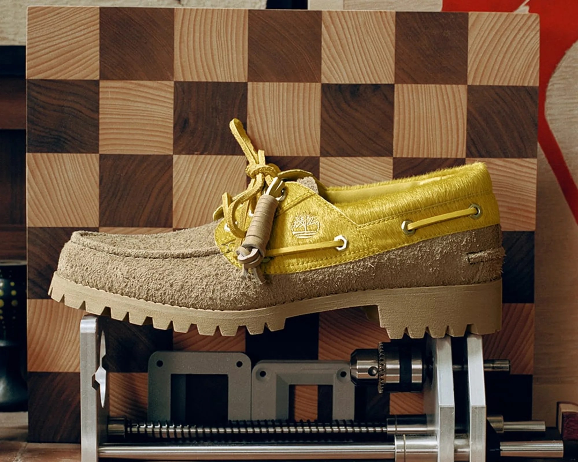Beige and yellow suede moccasin shoe with rugged sole on a metal and wood mechanical device.