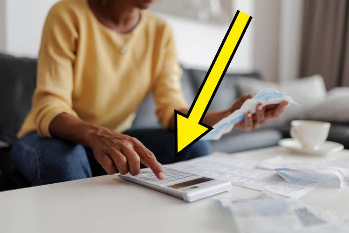 Person sitting on a couch, using a calculator and holding receipts on a table, with a cup in the background