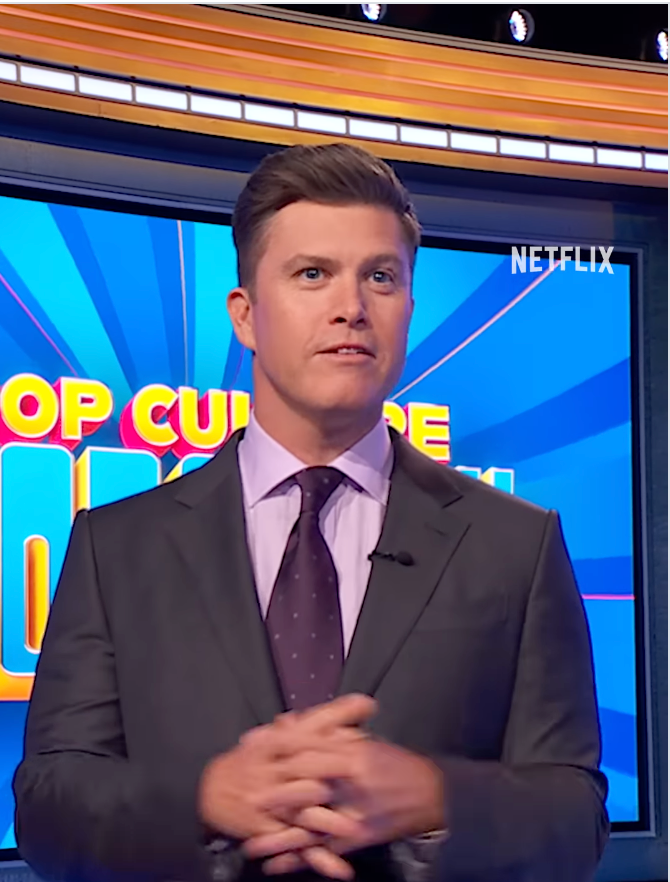 A person in a suit stands in front of a game show set with "Netflix" visible