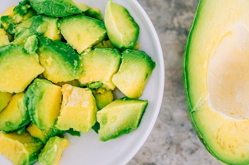 Bowl of diced avocado next to a halved avocado with the pit removed on a stone surface