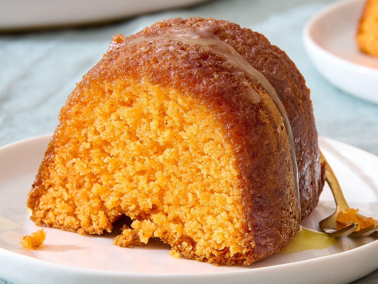 A slice of bundt cake on a white plate drizzled with syrup on top