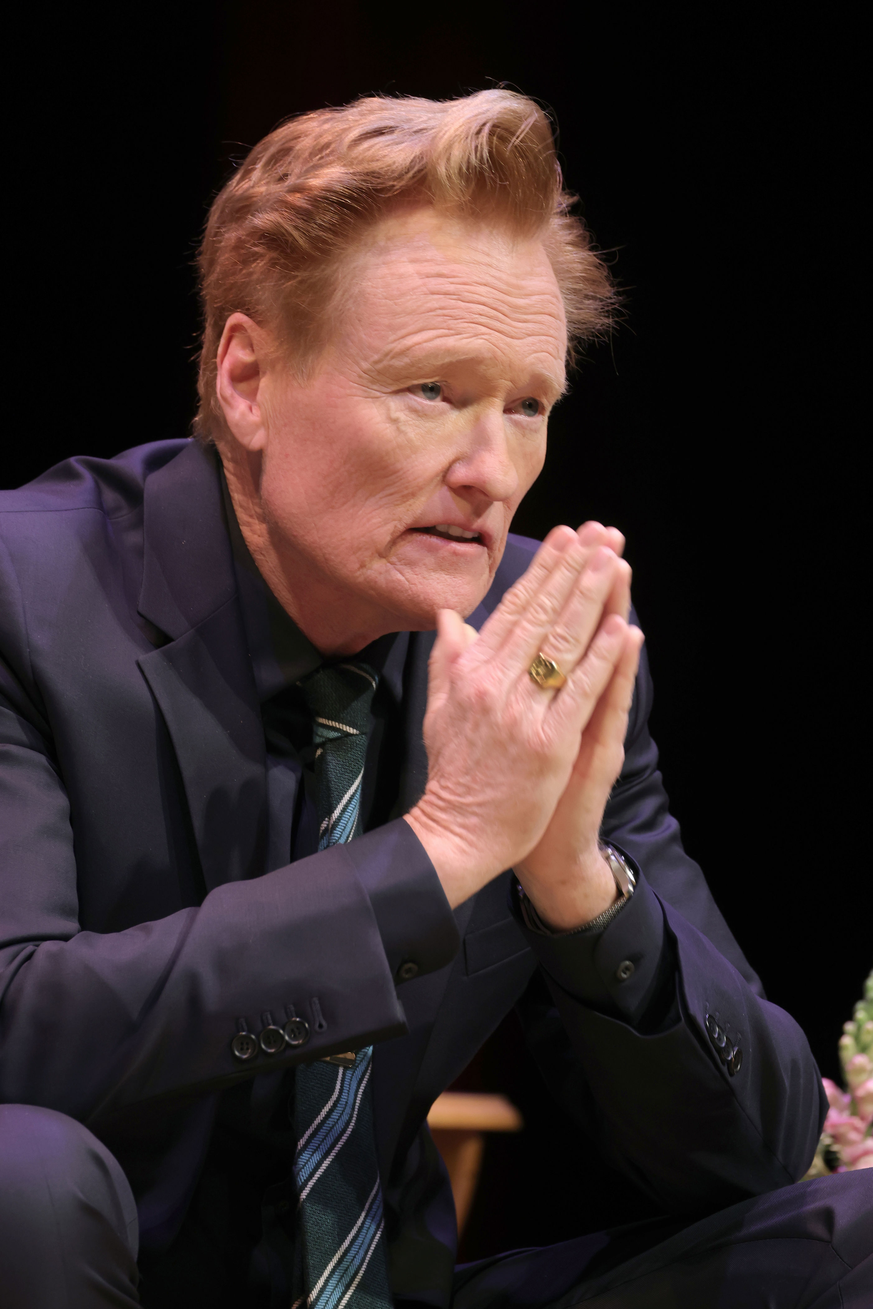 Conan O'Brien with clasped hands during a conversation.