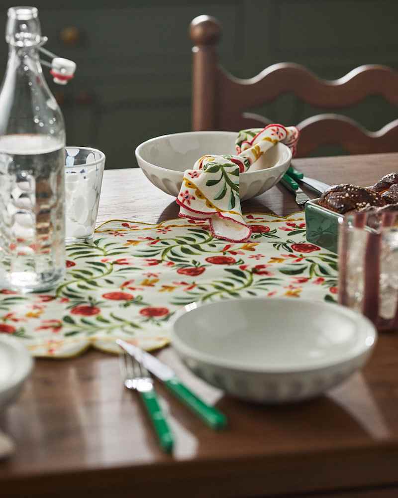 Table set with a floral tablecloth, glassware, white bowls, green-handled cutlery, and a dish of baked goods.