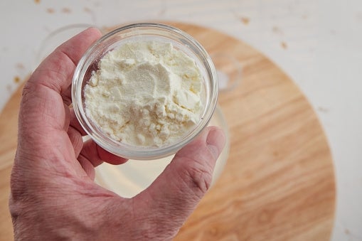 Hand holding a small bowl of powder over a wooden surface