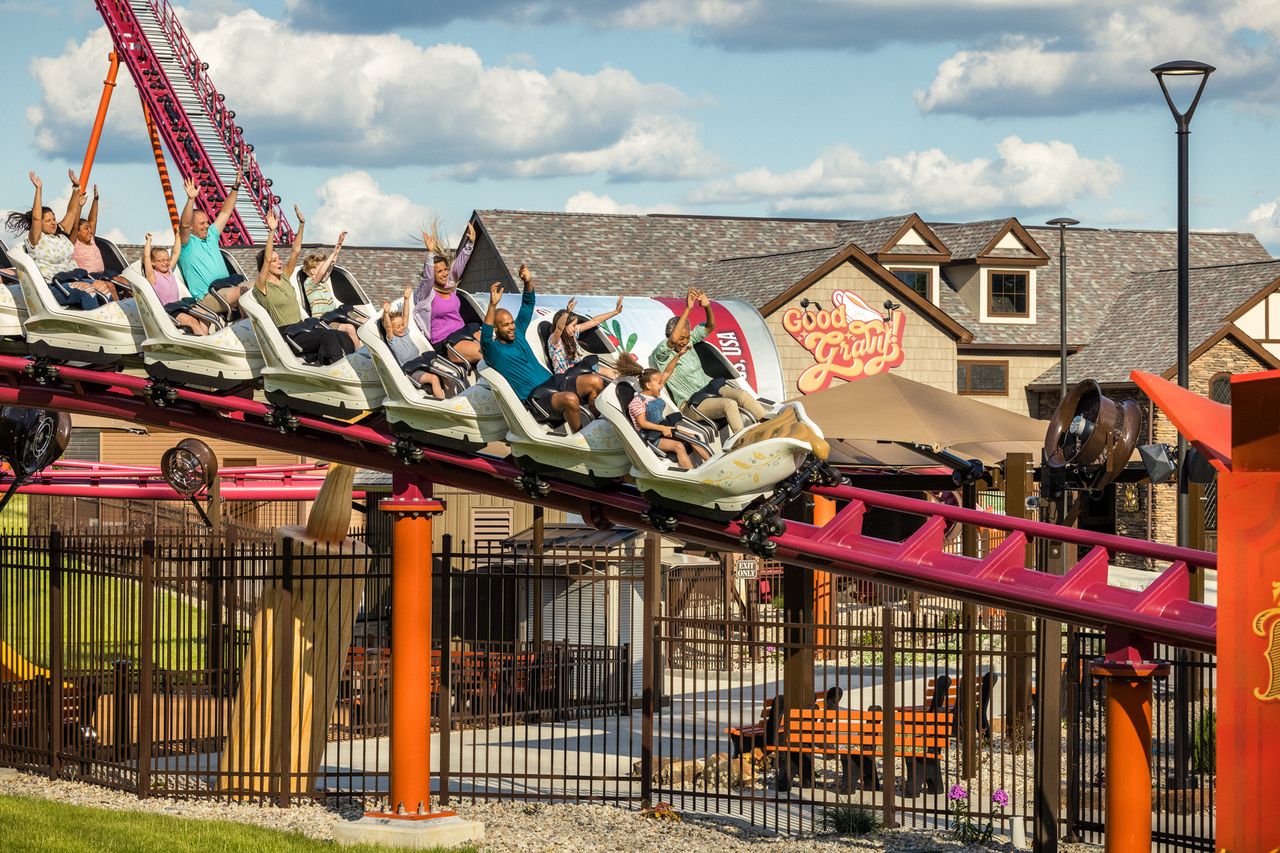 Group of people riding a roller coaster at an amusement park with buildings in the background