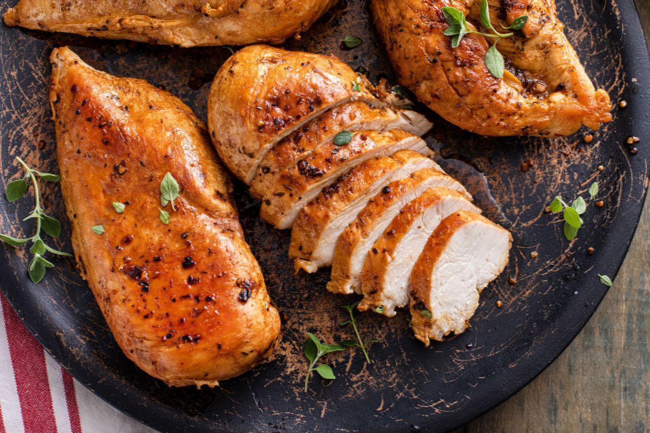 Cooked chicken breasts one sliced garnished with herbs on a dark plate