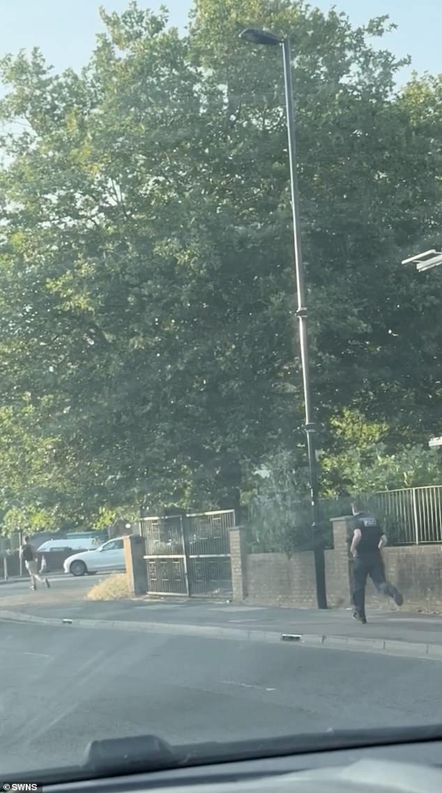 Footage shows a woman driving in her car - with a passenger filming the clip - as an officer sprints along the side of the road in pursuit of his target, who appears to be wearing shorts and a rucksack