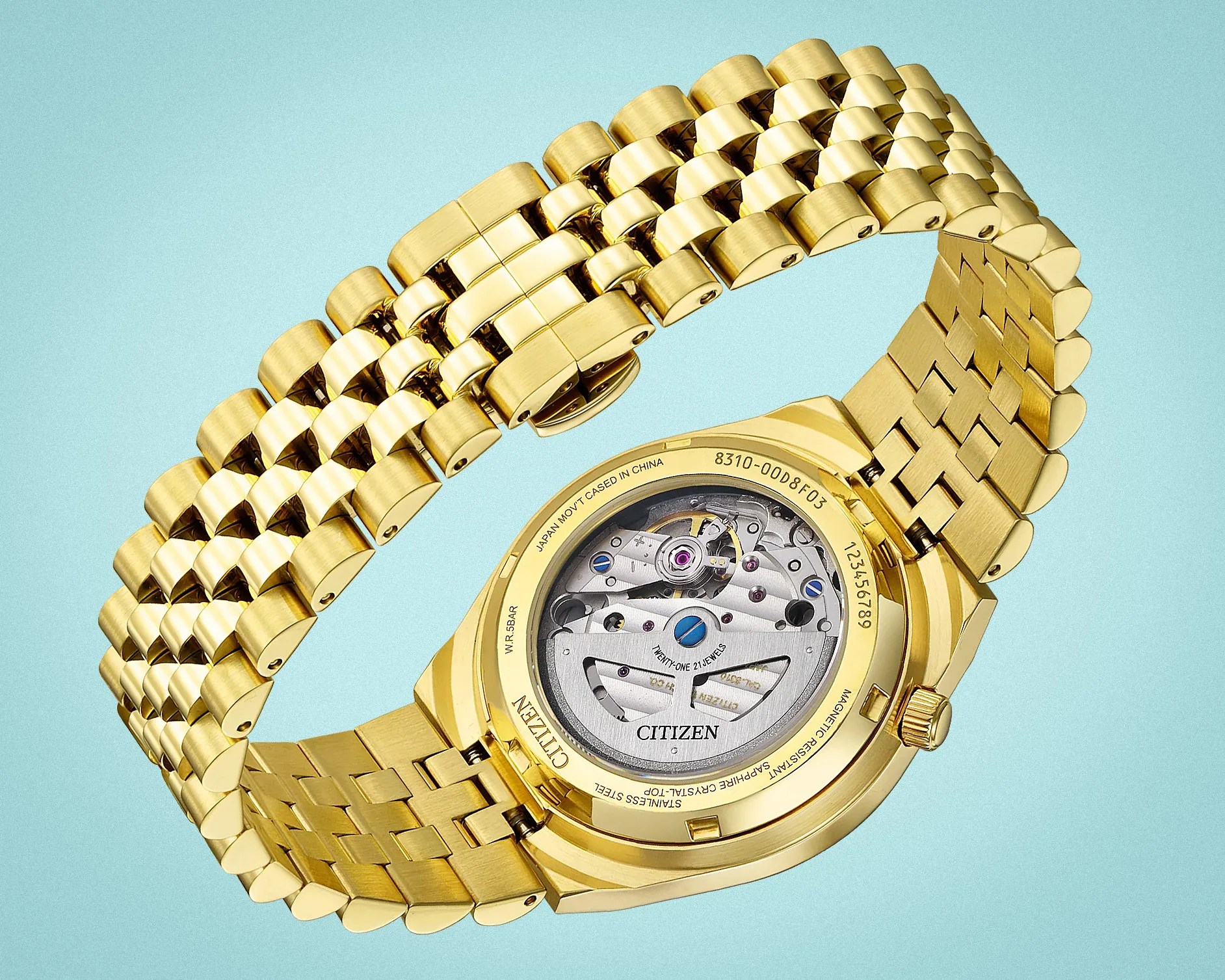 Gold-tone Citizen watch with visible mechanical movement and linked metal bracelet on a light blue background.