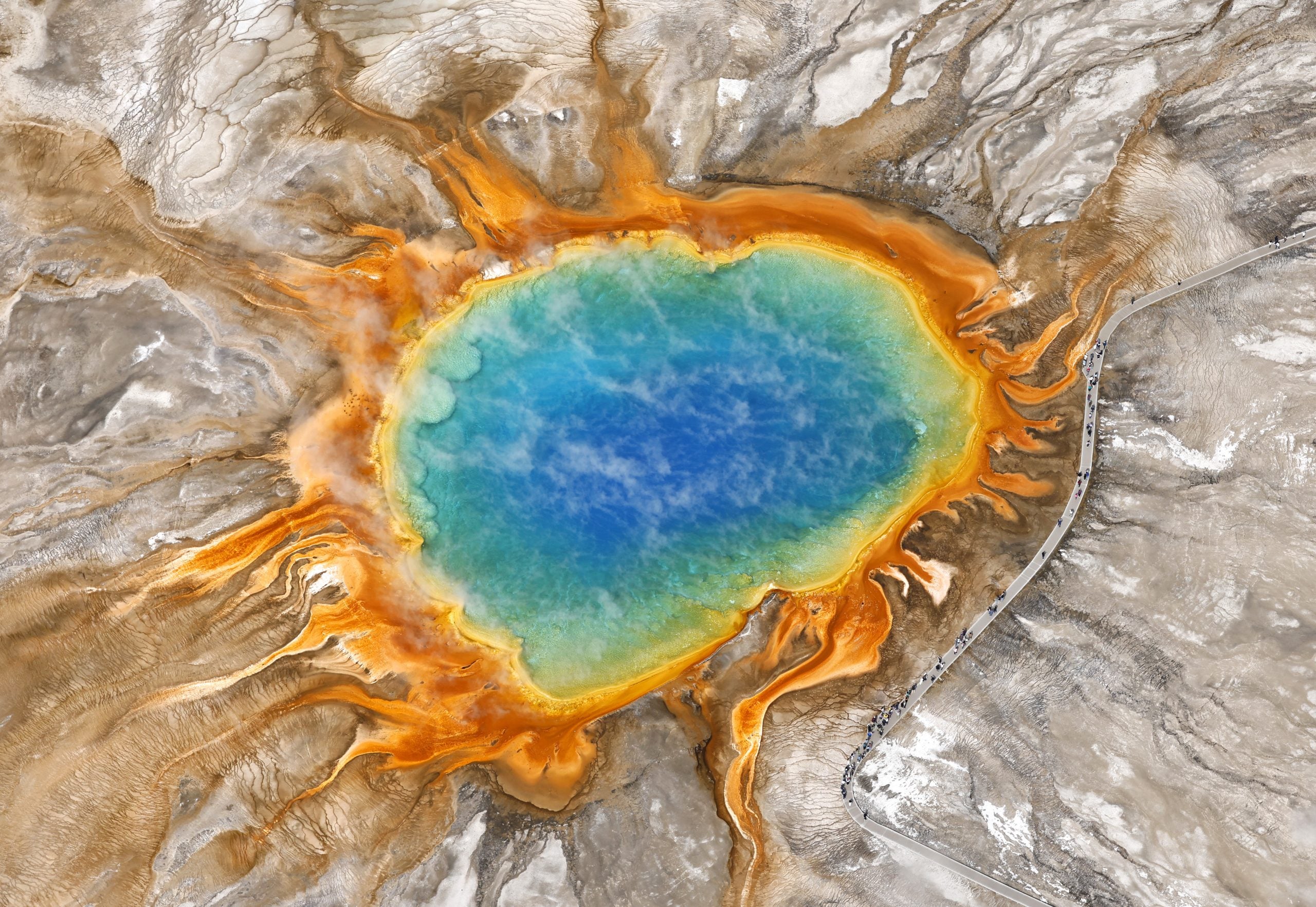 YELLOWSTONE NATIONAL PARK, WYOMING - MAY 24: An aerial view of visitors walking around Grand Prismatic Spring in the Midway Geyser Basin on May 24, 2026 in Yellowstone National Park, Wyoming. Grand Prismatic Spring is the largest hot spring in the United States at more than 300 feet wide at its widest point and over 120 feet deep. The colors outside the pool's blue center are created by 