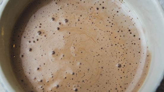 A close-up of a cup filled with frothy hot chocolate or coffee, showing bubbles on the surface