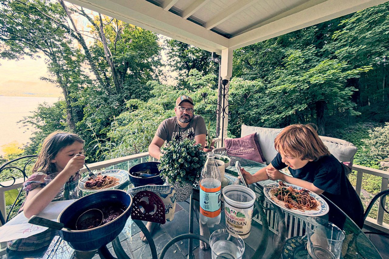 A family of three eating at an outdoor table surrounded by greenery on a covered patio