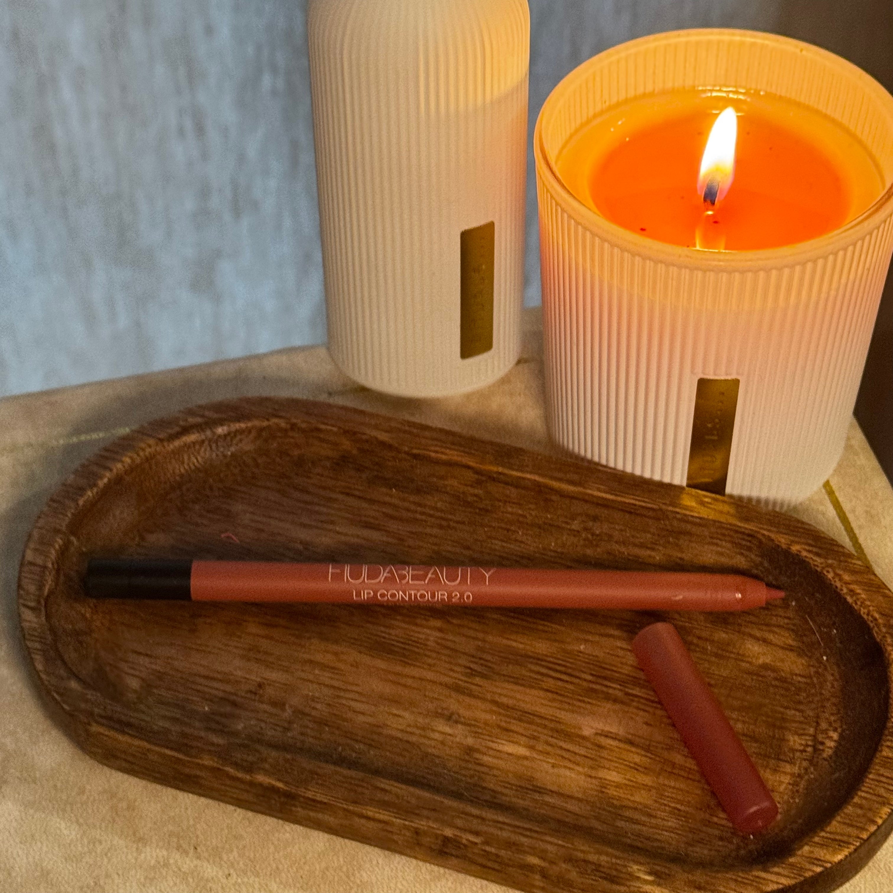 Lip liner on a wooden tray next to a lit candle and decorative containers, creating a cozy beauty setting