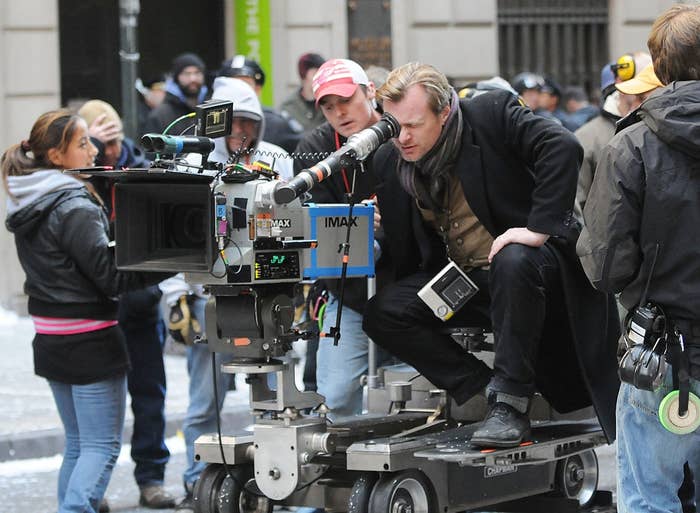 A film director looks through a camera on a busy set, surrounded by crew members