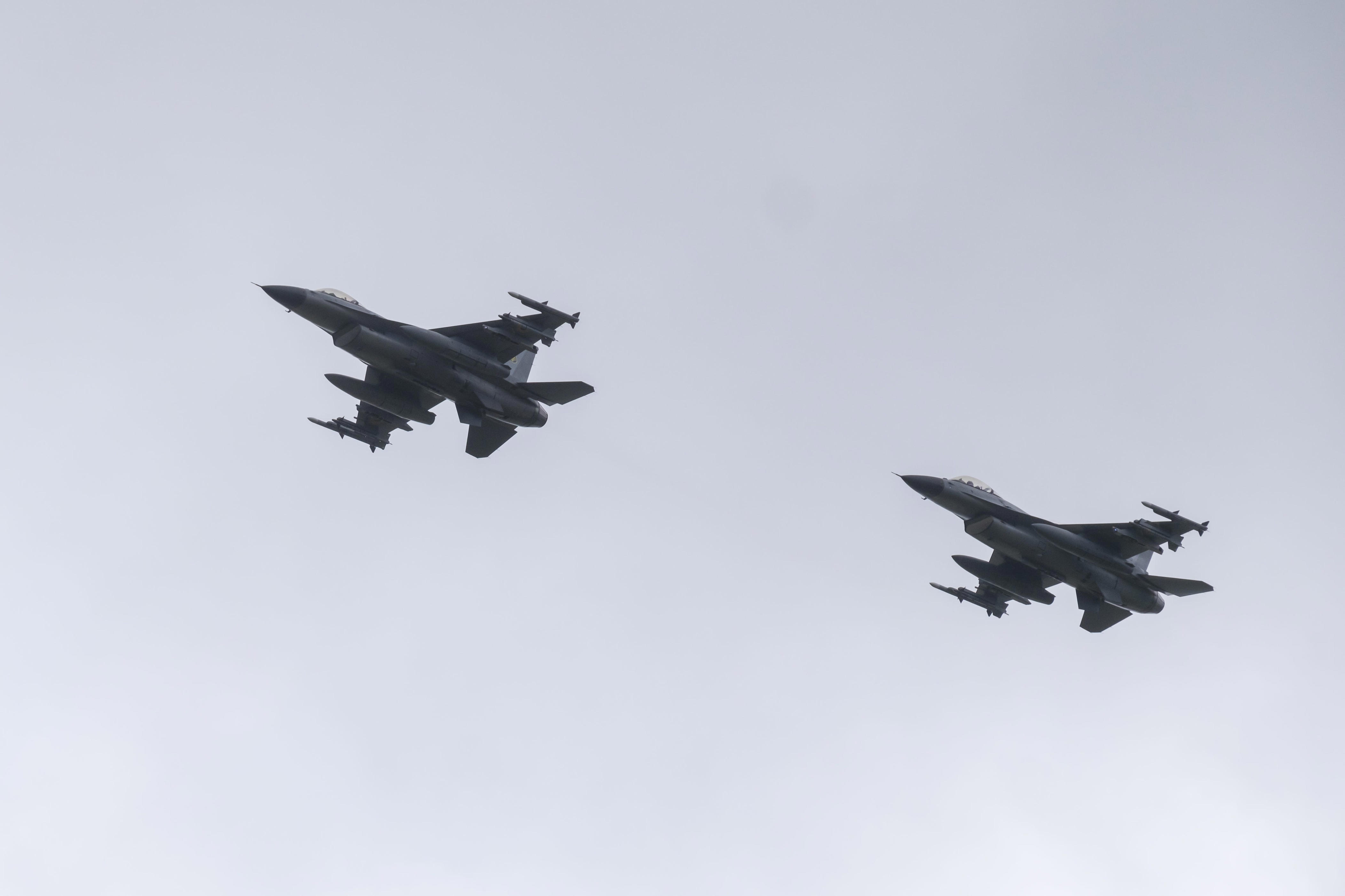Two military fighter jets fly in formation against an overcast sky.
