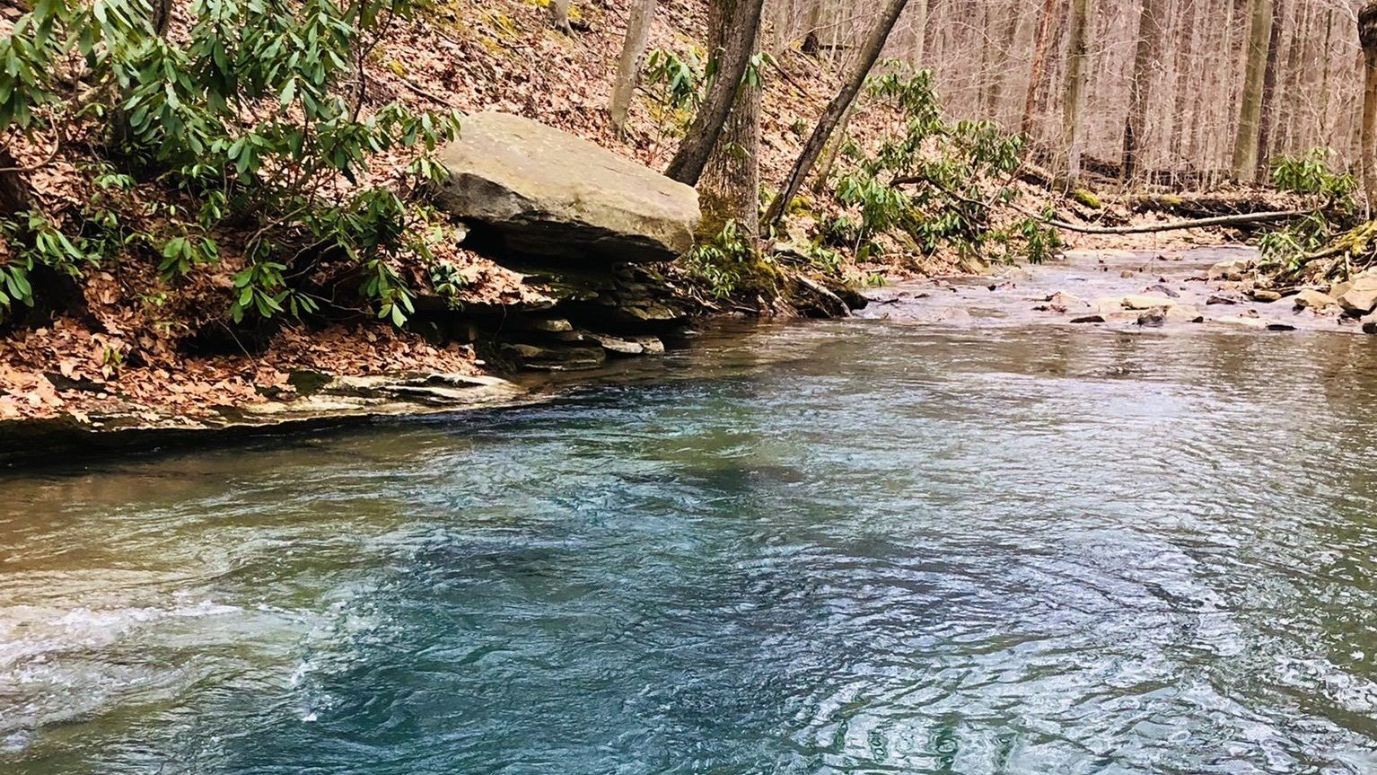 Views of Blue Hole, a beautiful swimming hole in Pennsylvania, surrounded by a rocky creek bed and woodlands.