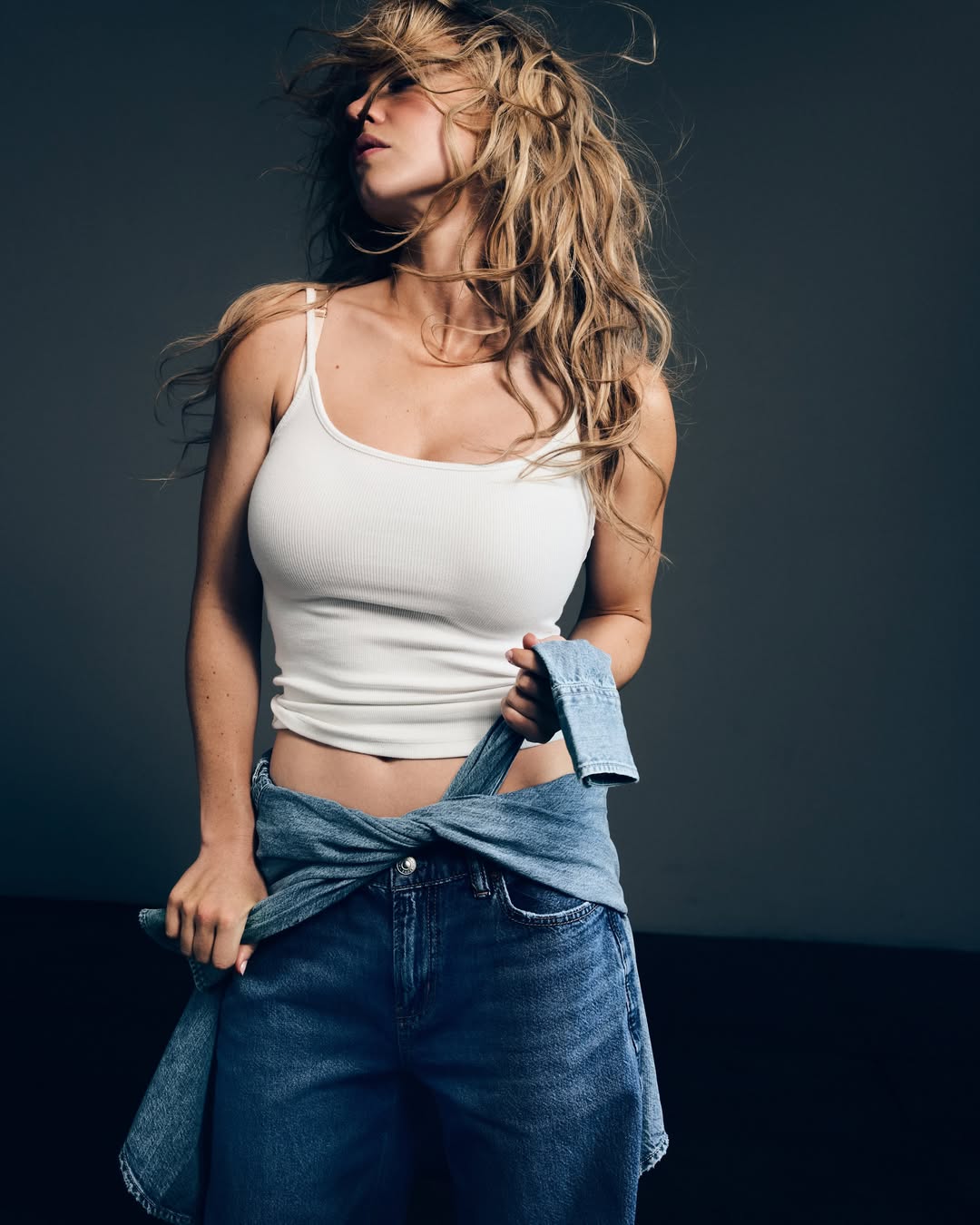 Sydney Sweeney in a white tank top and blue jeans, with a denim jacket tied around her waist.