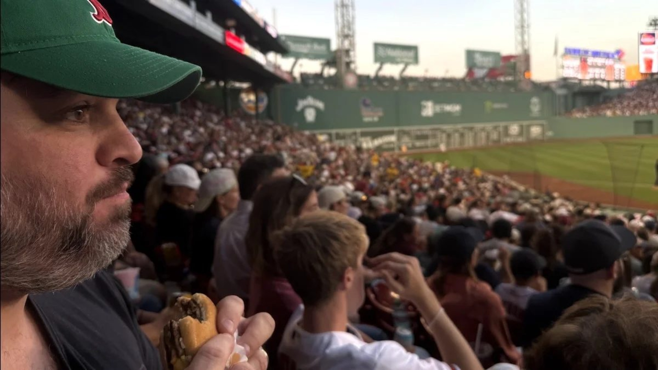 A bearded man in a green hat eating a McDouble at Fenway Park