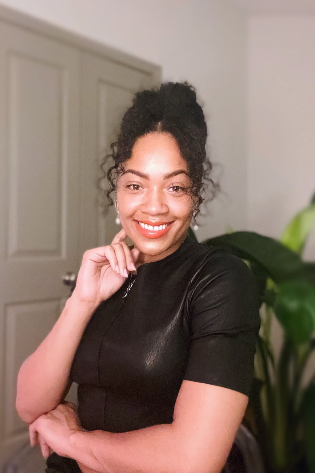 A smiling woman with curly dark hair tied up, wearing a black top.