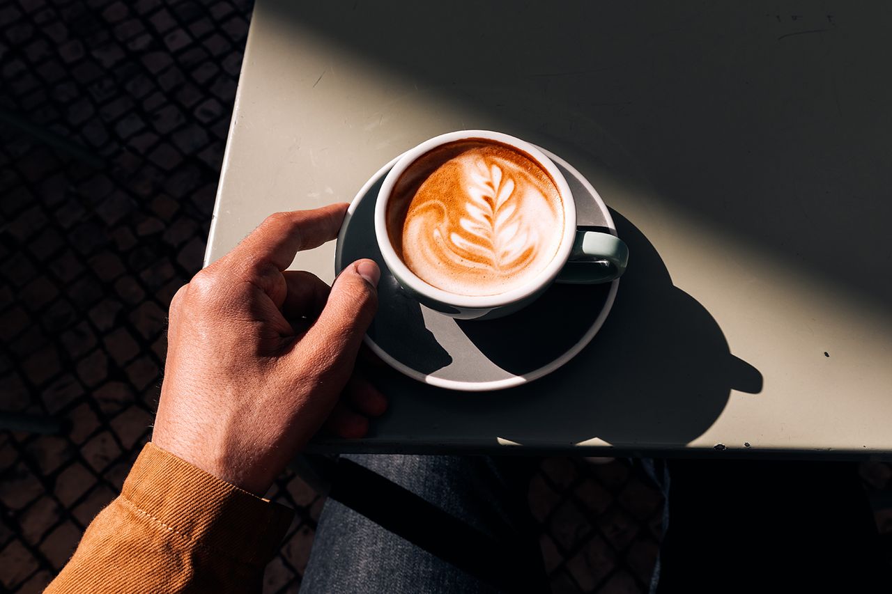 Man drinking latte at a sidewalk cafe on a sunny day, personal perspective view