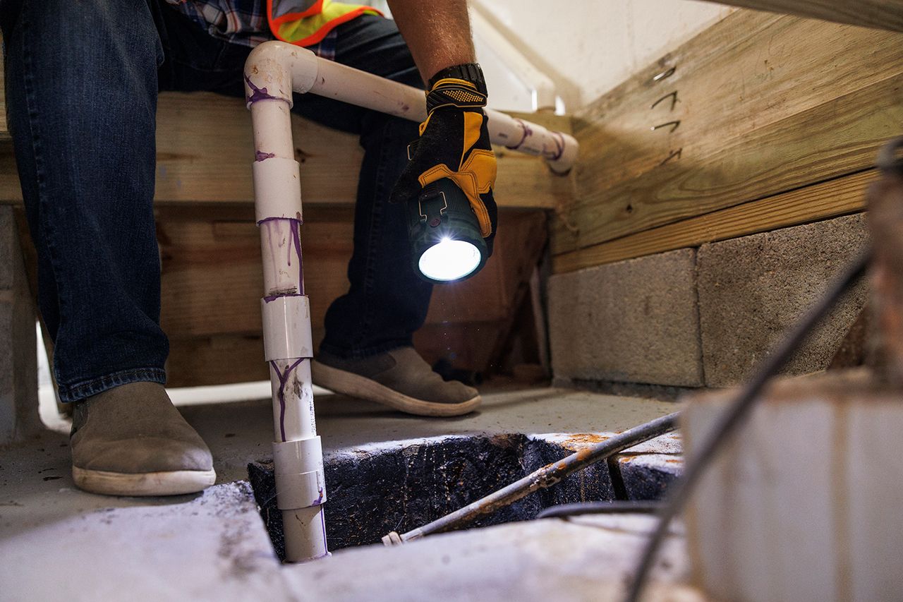 A person inspecting a sump pump installation in a basement