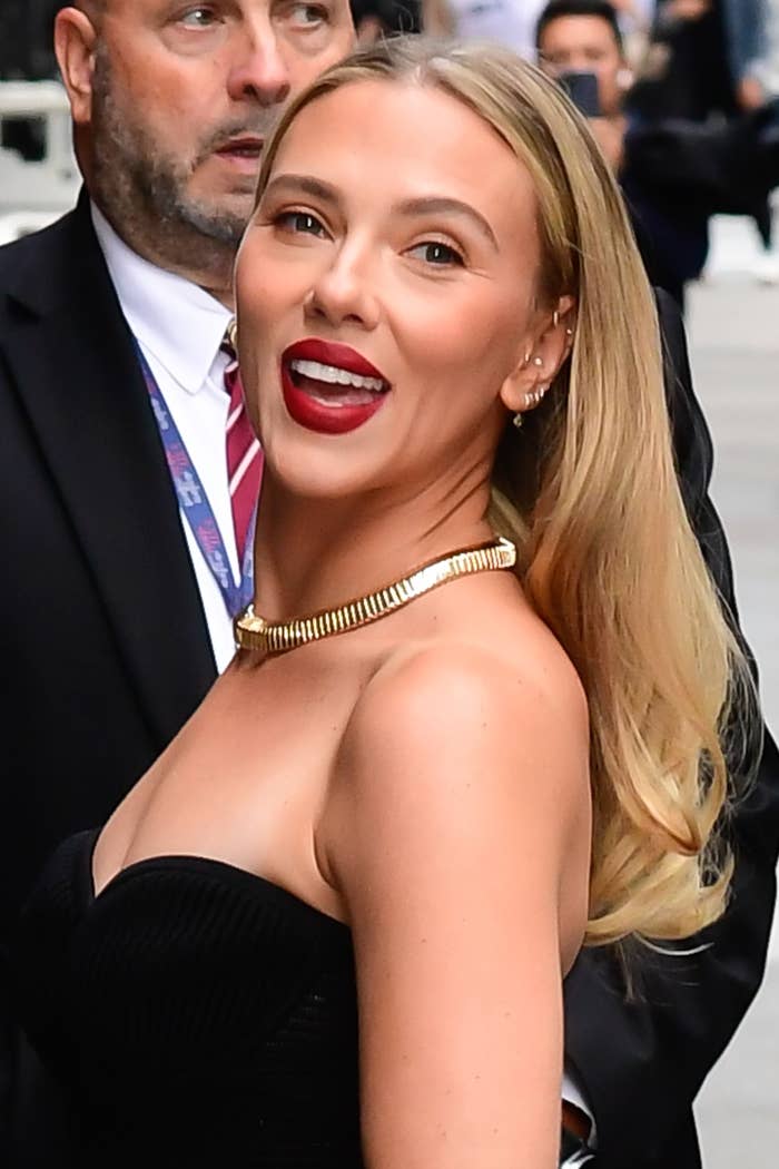 Person smiling, wearing a strapless black dress and a gold necklace