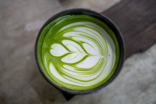 Artistic latte with a leaf design in frothy milk on top of green tea