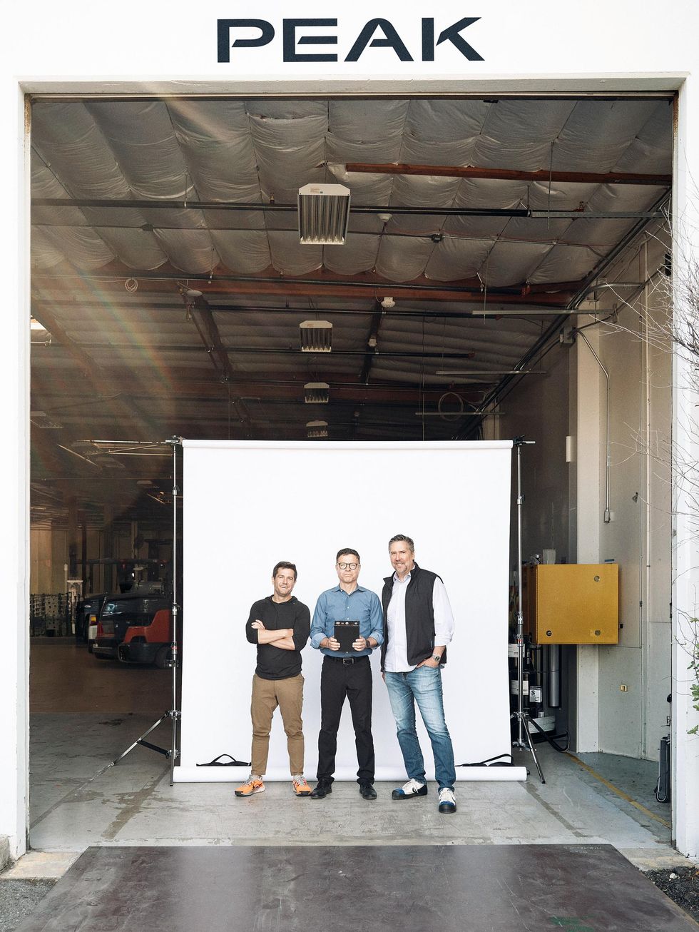 Three men standing together in a warehouse\u2019s entrance. The man at-center is holding a prismatic cell battery.