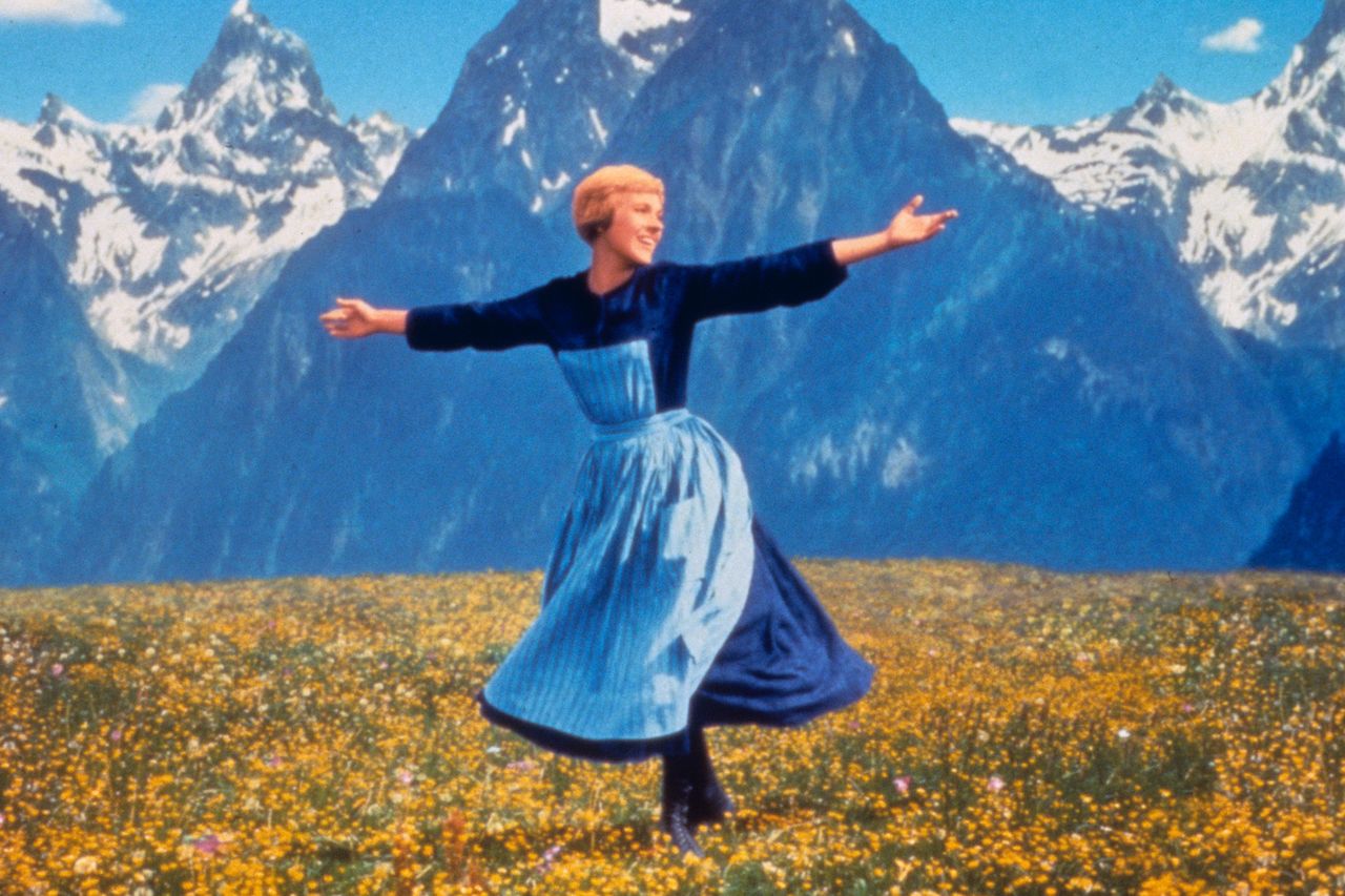 A person twirling in a field with mountains in the background