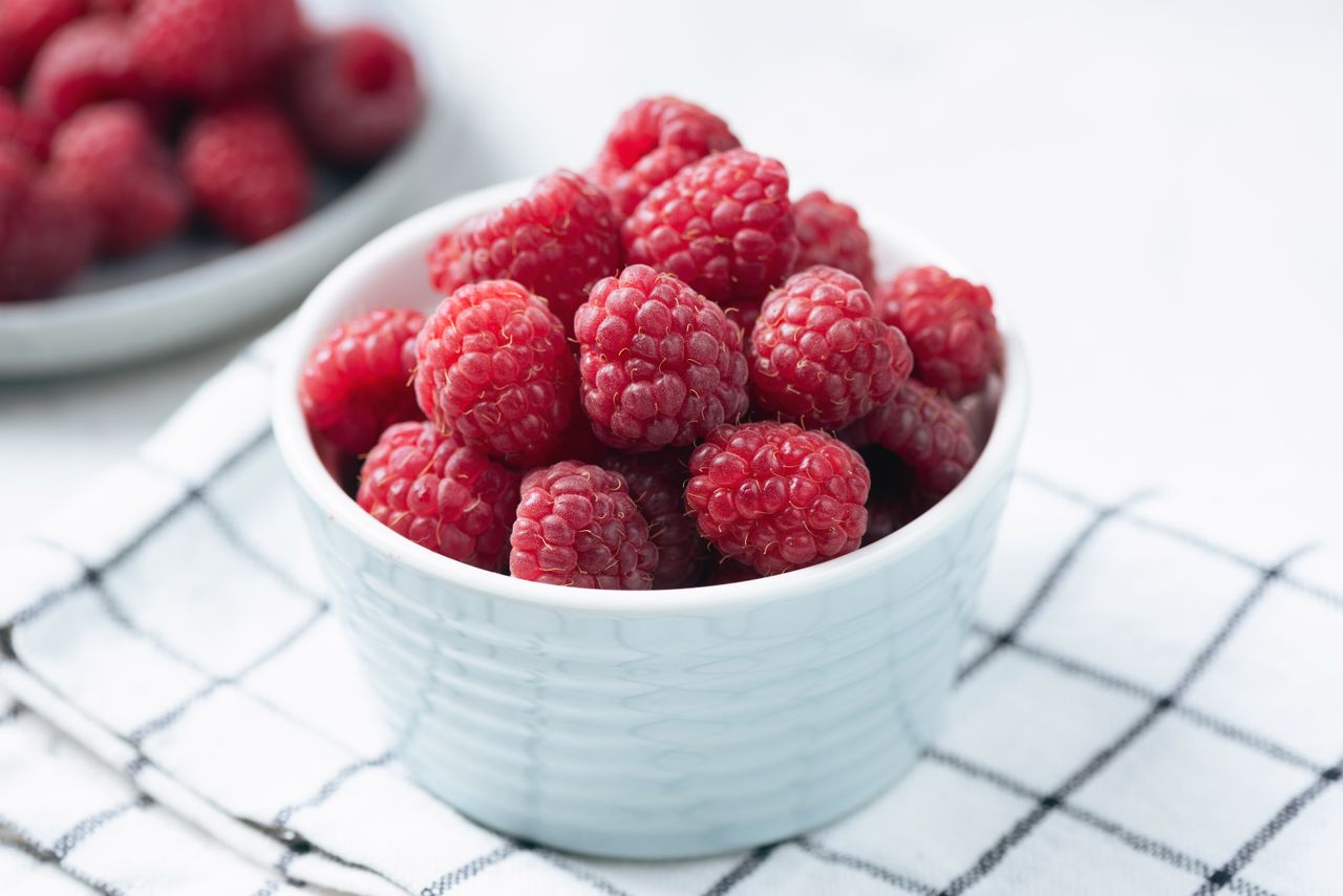 A bowl of raspberries on a checkered cloth