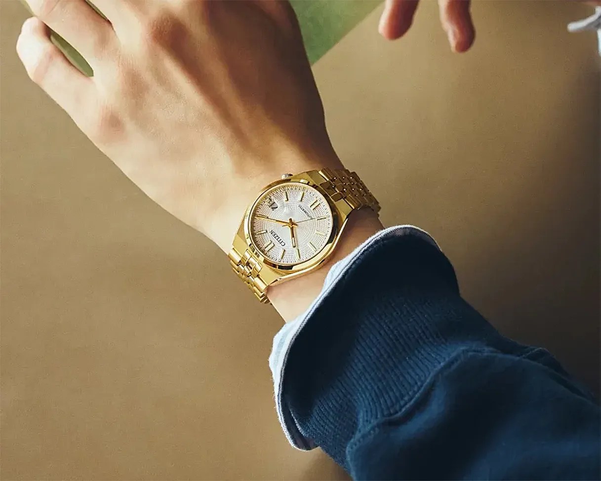Gold-tone Citizen wristwatch with a white textured dial and metal link bracelet worn on a wrist.