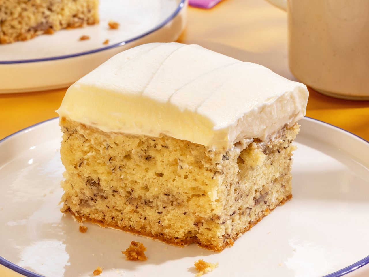 Slice of banana cake with thick white frosting on plate.