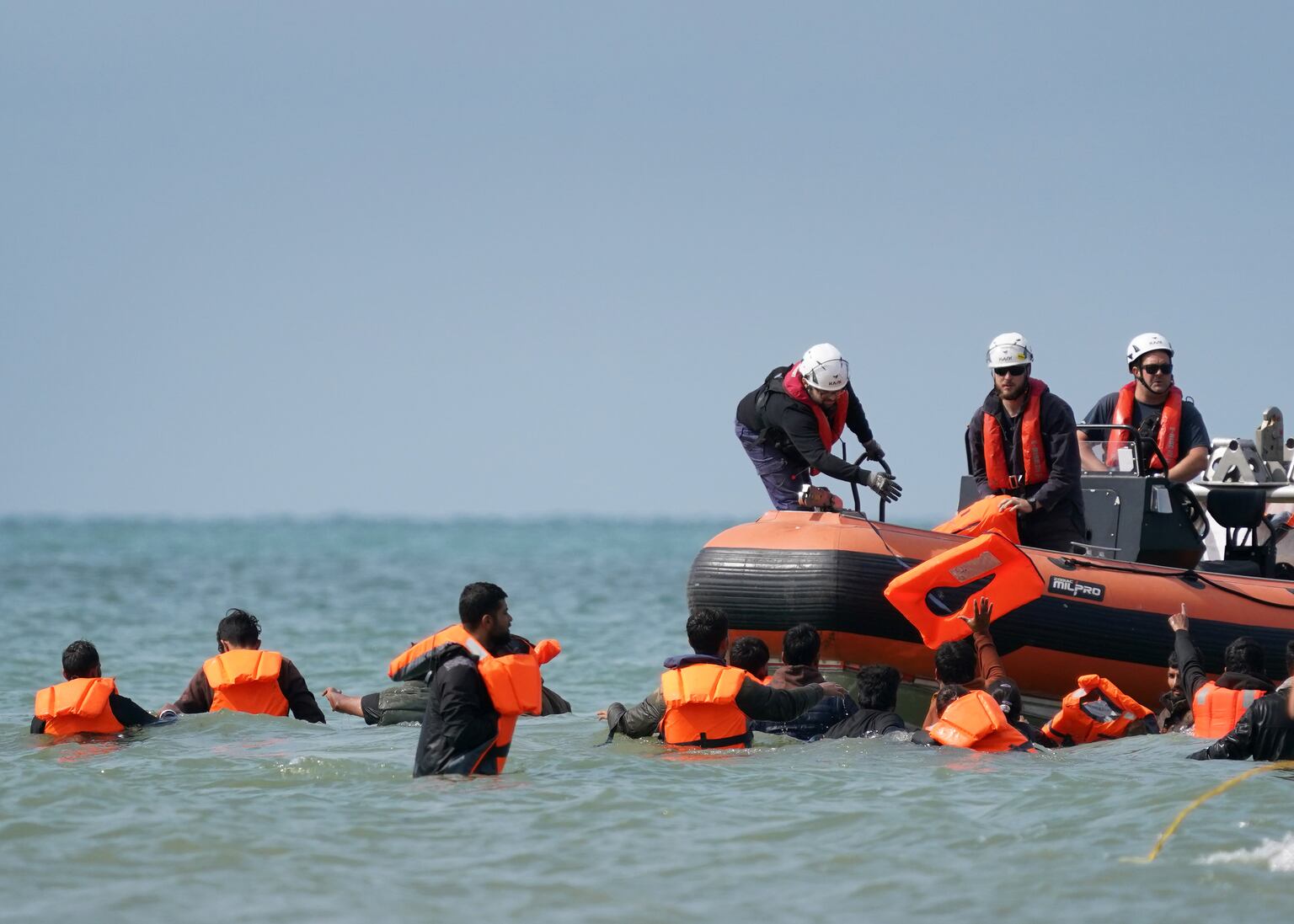 People thought to be migrants are handed life vests by French rescuers as they wade through the sea to board a small boat off the coast of Equihen-Plage