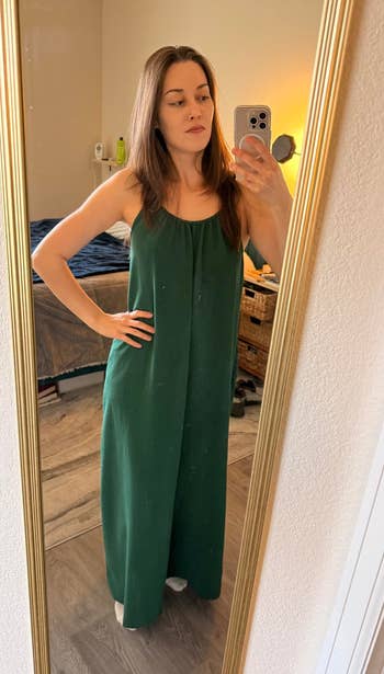 Person wearing a sleeveless, floor-length dress takes a mirror selfie in a bedroom