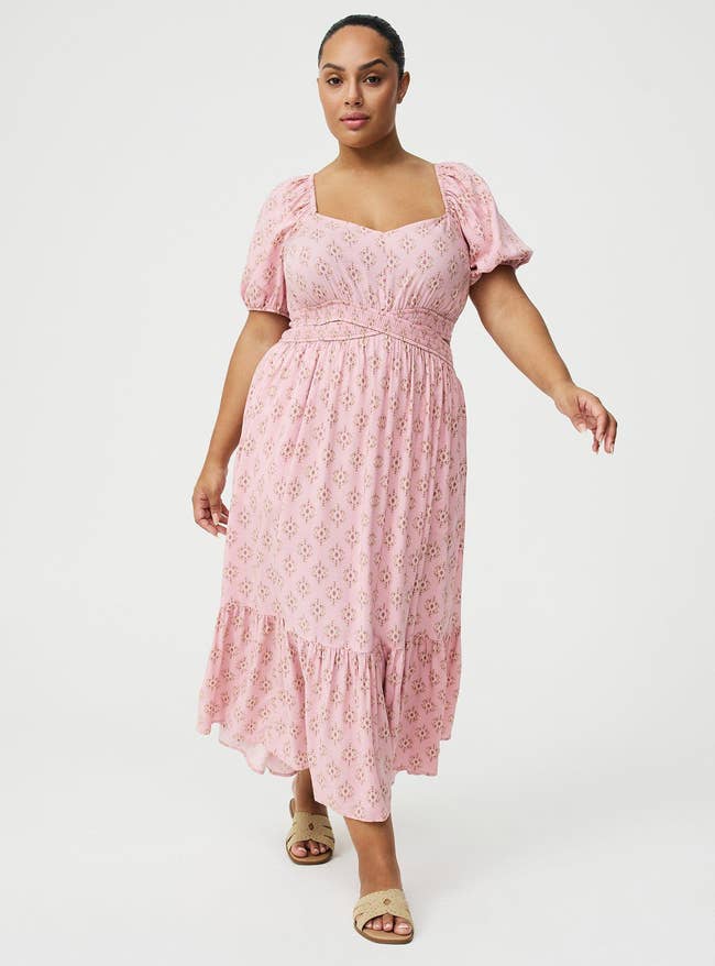 A person poses in a floral-patterned, puff-sleeve dress. They are wearing sandals. Image suitable for a shopping article