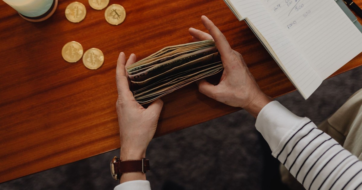Close-up of a person organizing money with cryptocurrency coins on a wooden table, symbolizing modern finance.
