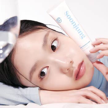 Person holding a Soonjung skincare product near their face, lying down, showcasing smooth skin for a beauty and shopping article