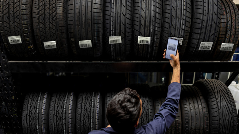 An employee using a smartphone to scan the codes of new tires on a rack
