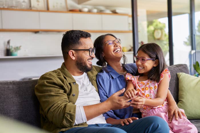 A joyful family of three, sitting on a couch, laughing together in a bright, modern living room