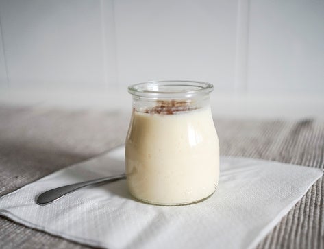 A jar of pudding sits on a napkin with a spoon beside it on a table, showcasing a simple dessert presentation