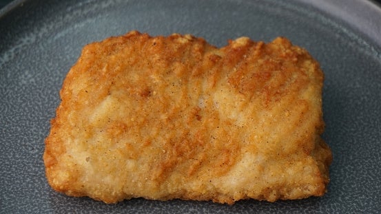 Breaded and fried fish fillet on a grey plate, showing a crispy texture