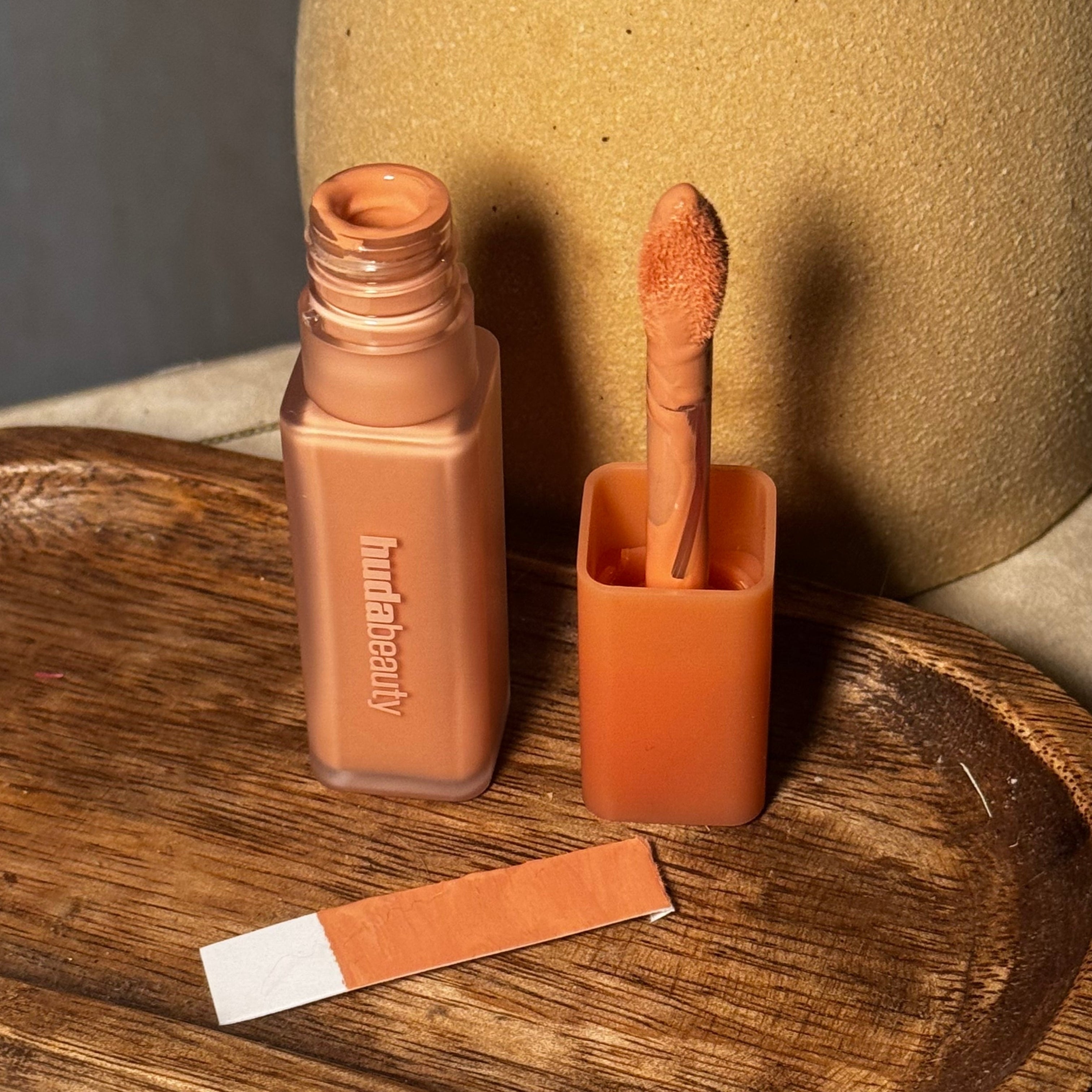 Concealer with applicator on a wooden tray, next to a matching paint swatch, suggesting a beauty or makeup theme