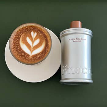 A cup of cappuccino with latte art beside a silver-toned bottle labeled
