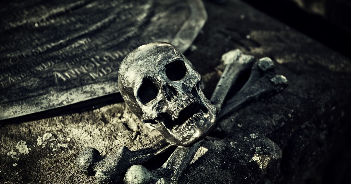 A haunting close-up of a skull and crossbones on an ancient tombstone in a spooky cemetery.