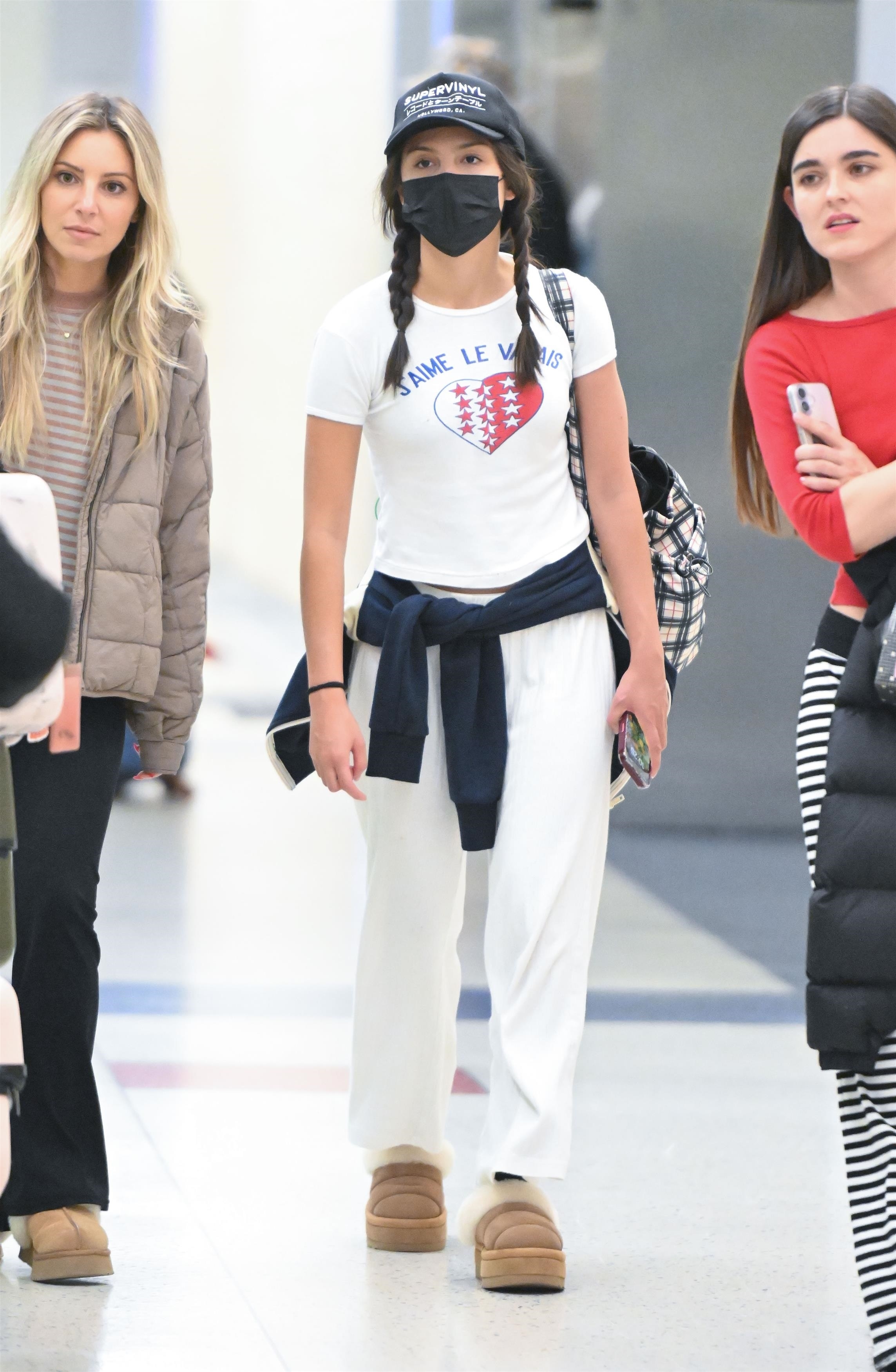 Olivia Rodrigo was spotted arriving back in the United States at JFK in New York after a trip in Iceland.. She wore a white graphic T-shirt, Leset Nando white pants, and Ugg Tazzlita mules.