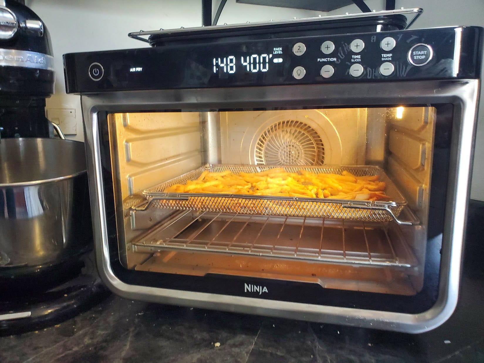 Fries cook in the Ninja Foodi XL Pro Air Fry Oven on a kitchen counter.