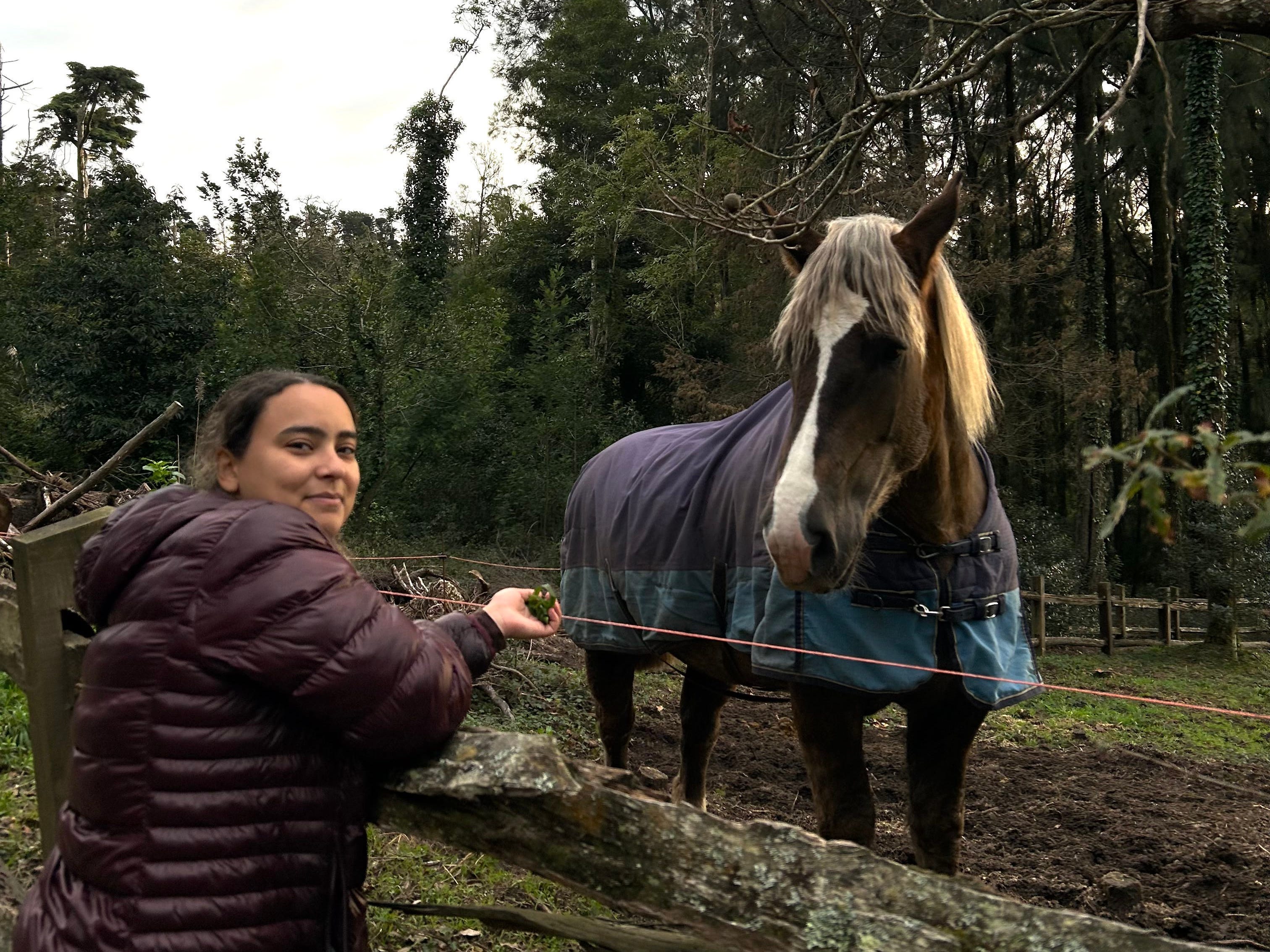 The writer wearing a puffer coat and standing near a horse in Sintra, Portugal.