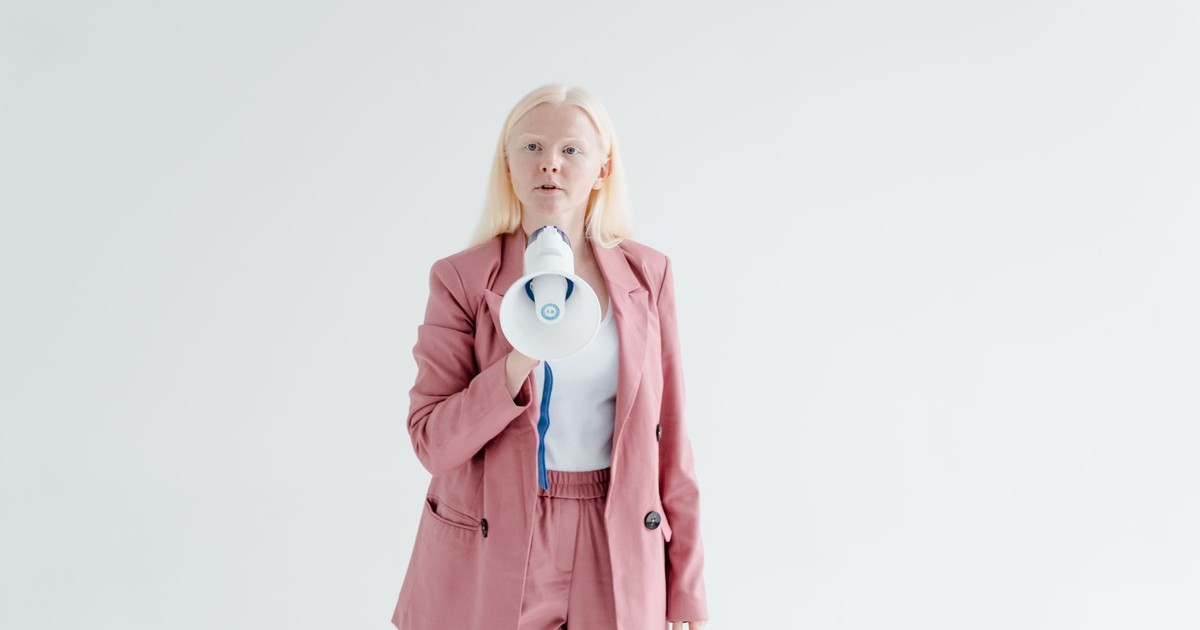 Portrait of a confident woman in a pink suit holding a megaphone on a white background, promoting leadership and empowerment.