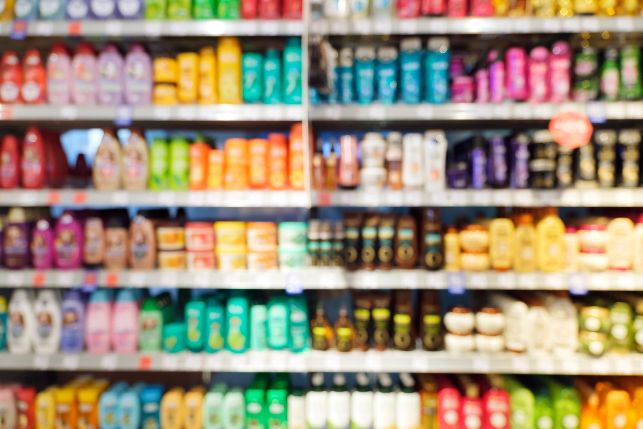 Blurred image of a store shelf filled with various shampoo and conditioner bottles in different shapes and sizes