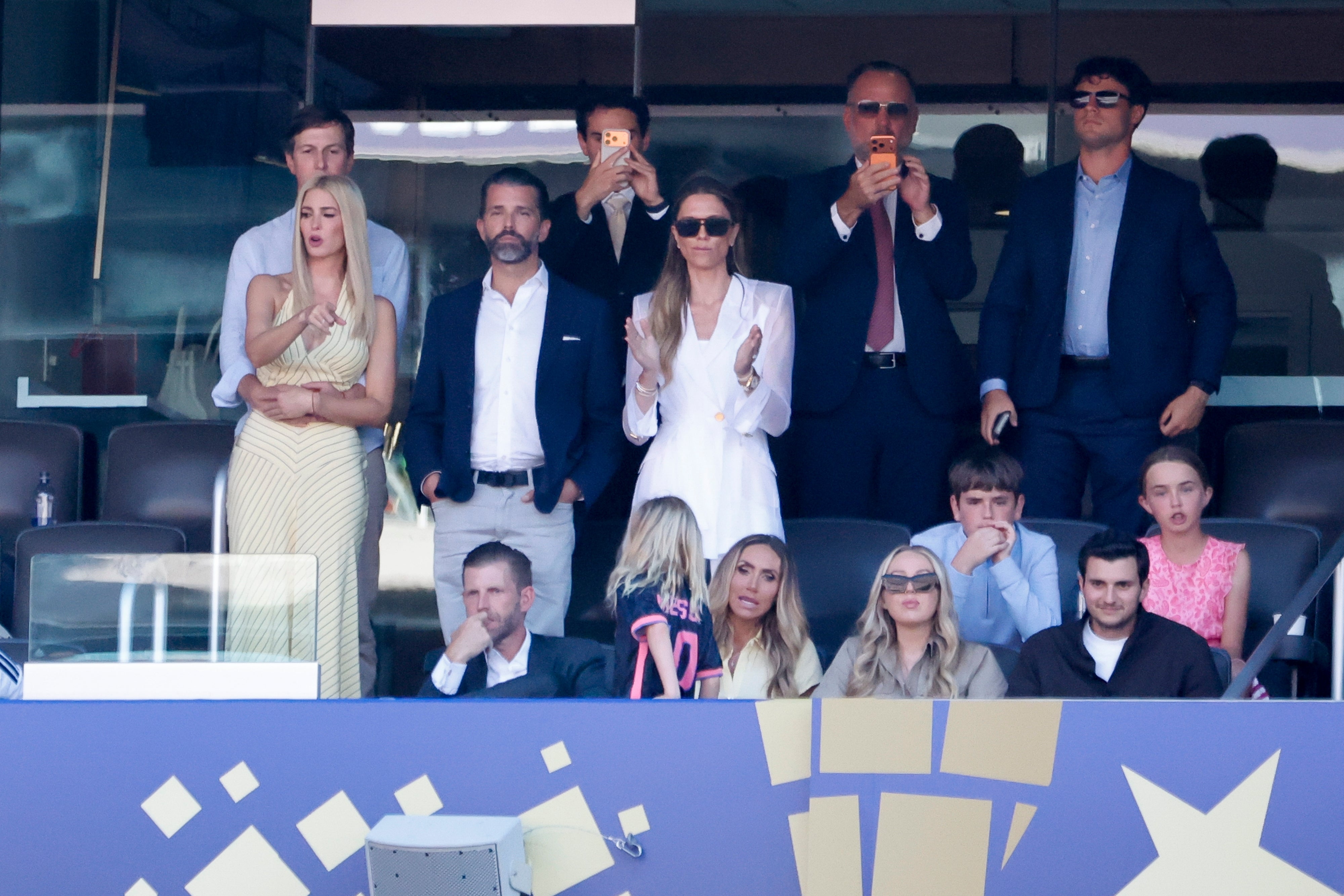 People in a stadium box, some standing and clapping while others sit