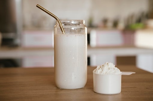 A glass of smoothie with a metal straw next to a scoop of protein powder on a wooden table